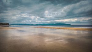 Ein großer flacher Strand an der Nordseeküste, der Himmel ist düster und bewölkt.