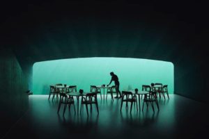 Unterwasserrestaurant mit großer Glasscheibe und Stühlen im Vordergrund.