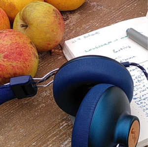 Blaue Kopfhörer liegen neben Äpfeln auf einem Holztisch