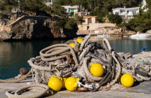 Mehrere Fischereinetze liegen aufeinandergestabelt an einem Hafen