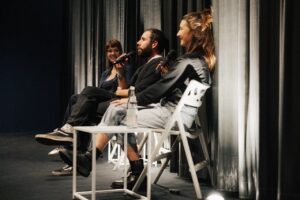 zwei Frauen und ein Mann auf Stühlen bei einer Podiumsdiskussion in einem Kino, lachend
